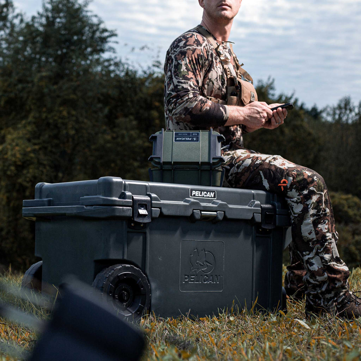 Charcoal Pelican 80QT Elite Wheeled Cooler in charcoal being used as a seat outside during a hunt