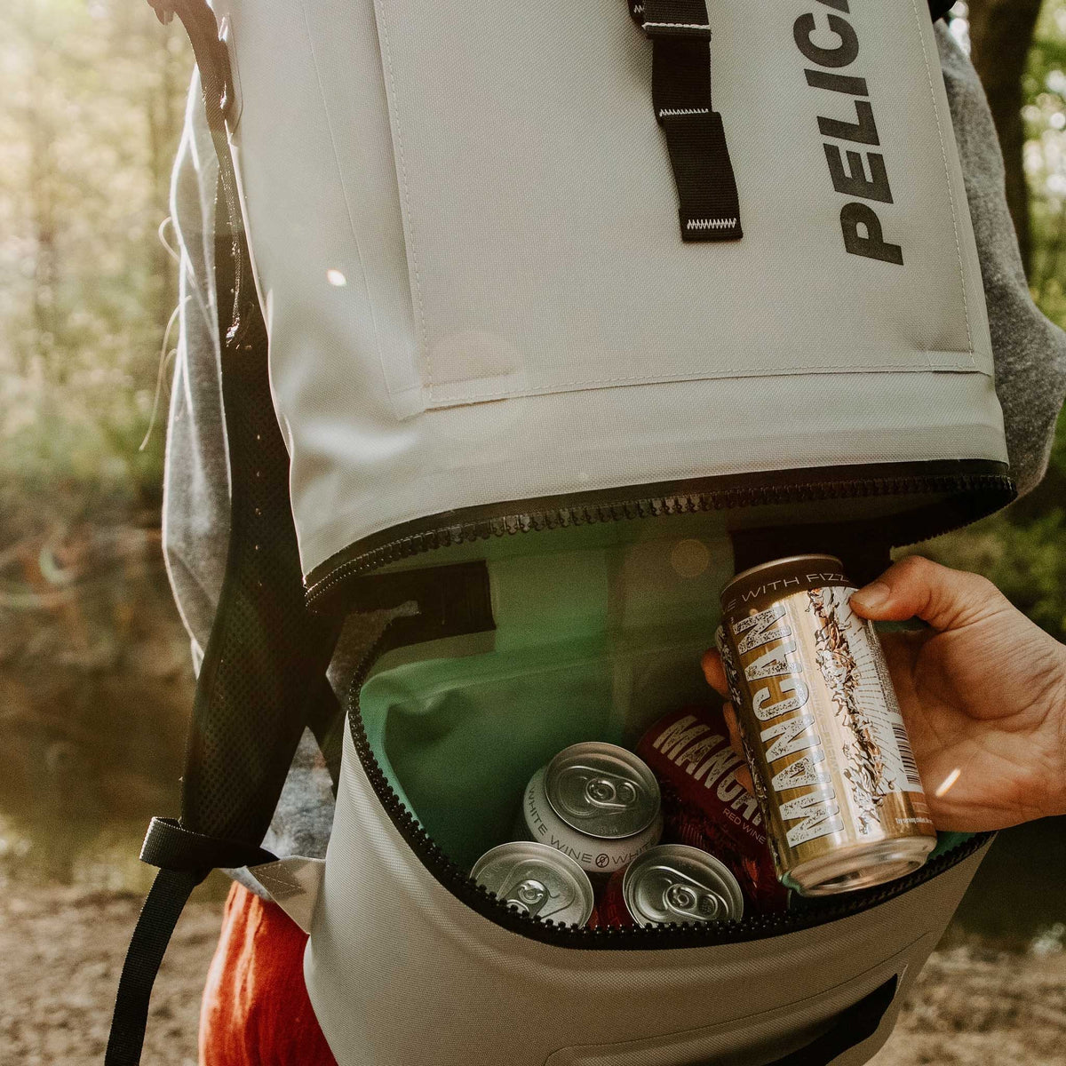 Light Grey Pelican™ Dayventure Backpack Soft Cooler canned beverages being pulled out of the cooler compartment