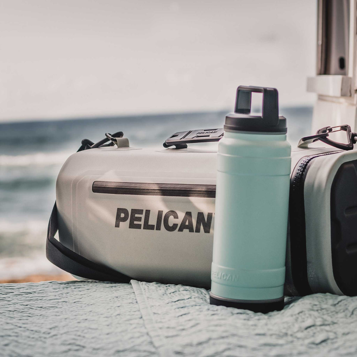 Light Grey Pelican™ Dayventure Sling Soft Cooler on the beach with a 32oz Pelican Bottle